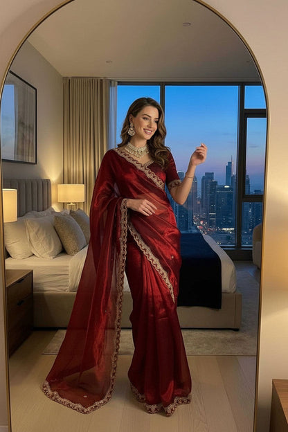 Woman in a red saree taking a mirror selfie in a room with city skyline view.