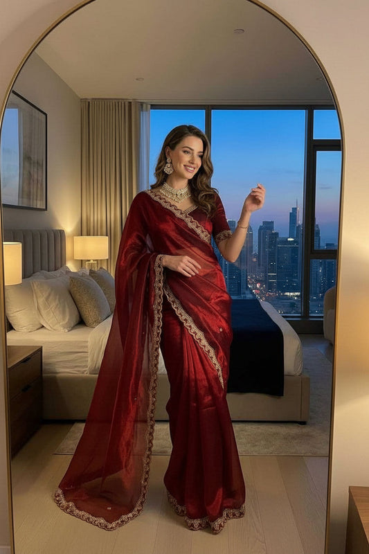 Woman in a red saree taking a mirror selfie in a room with city skyline view.