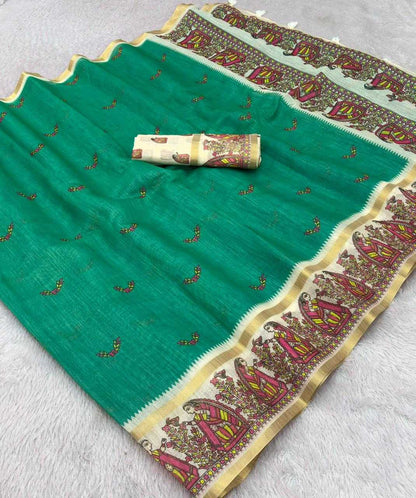 A green silk saree with a wide gold and multicolor border, featuring small gold and red floral motifs, with a matching rolled beige blouse piece placed on top.