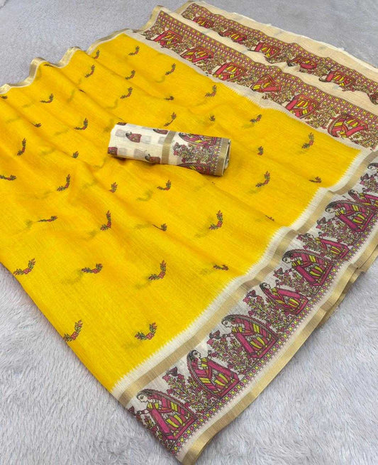 A bright yellow saree fabric with small embroidered motifs and a wide decorative border in beige, pink, and red, shown laid flat with a rolled matching section on a light gray textured surface.
