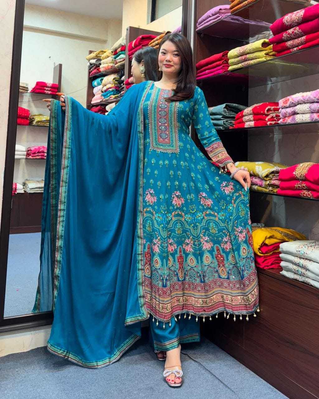 Woman in a blue embroidered traditional outfit standing in a fabric store.