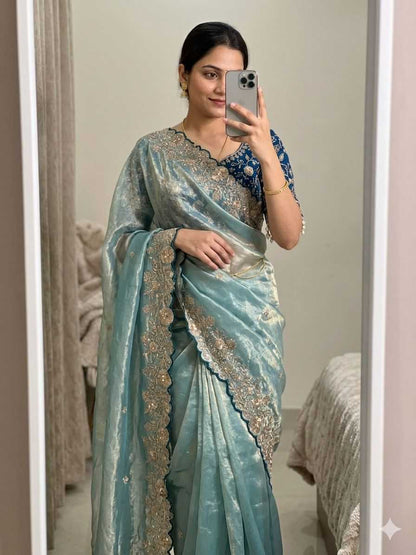 Woman wearing a light blue saree with intricate designs, taking a mirror selfie.