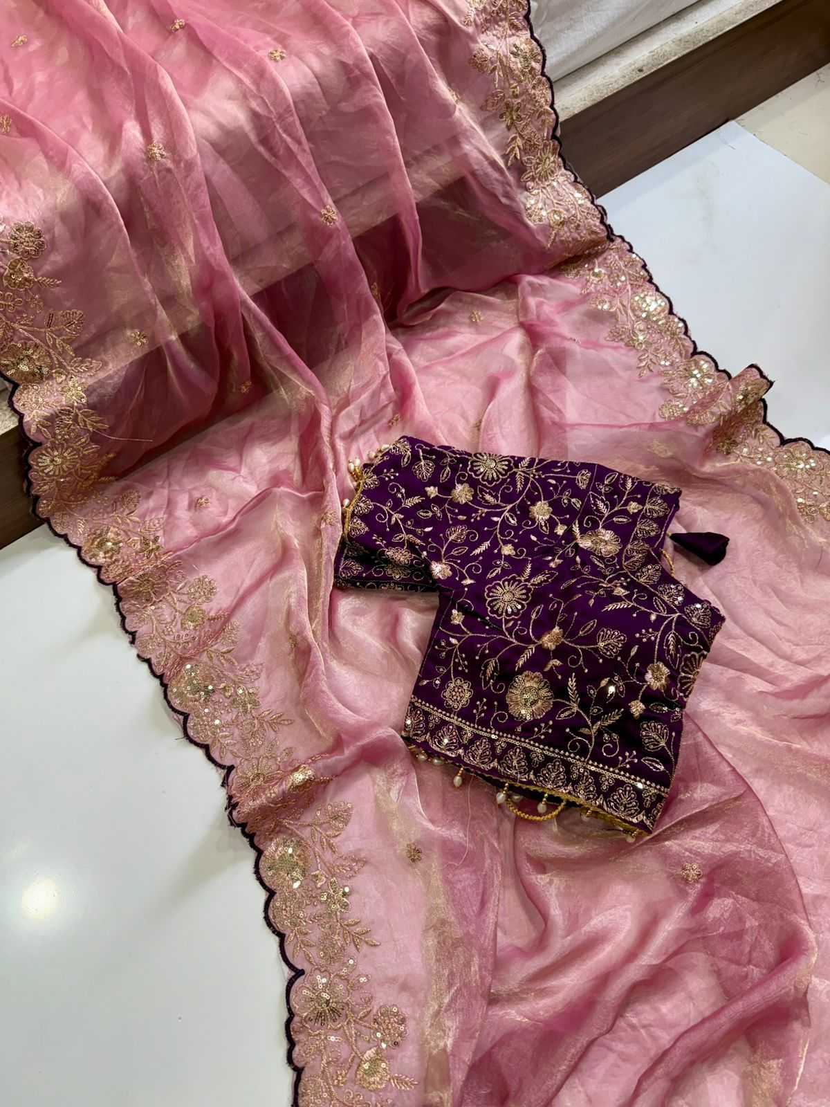Pink saree with gold embroidery and a purple blouse with gold detailing on a white surface.