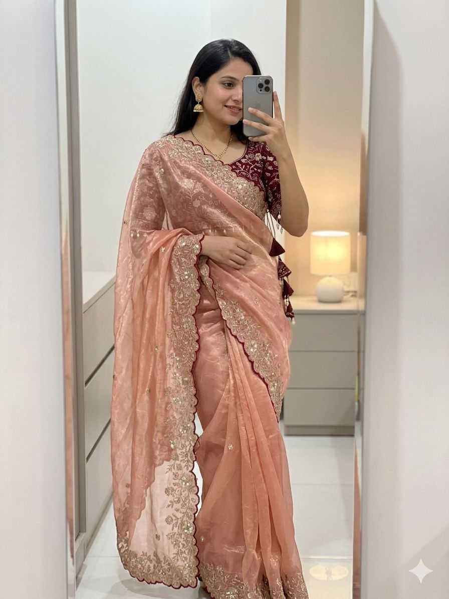 Woman wearing a pink saree with intricate designs, standing in front of a mirror.