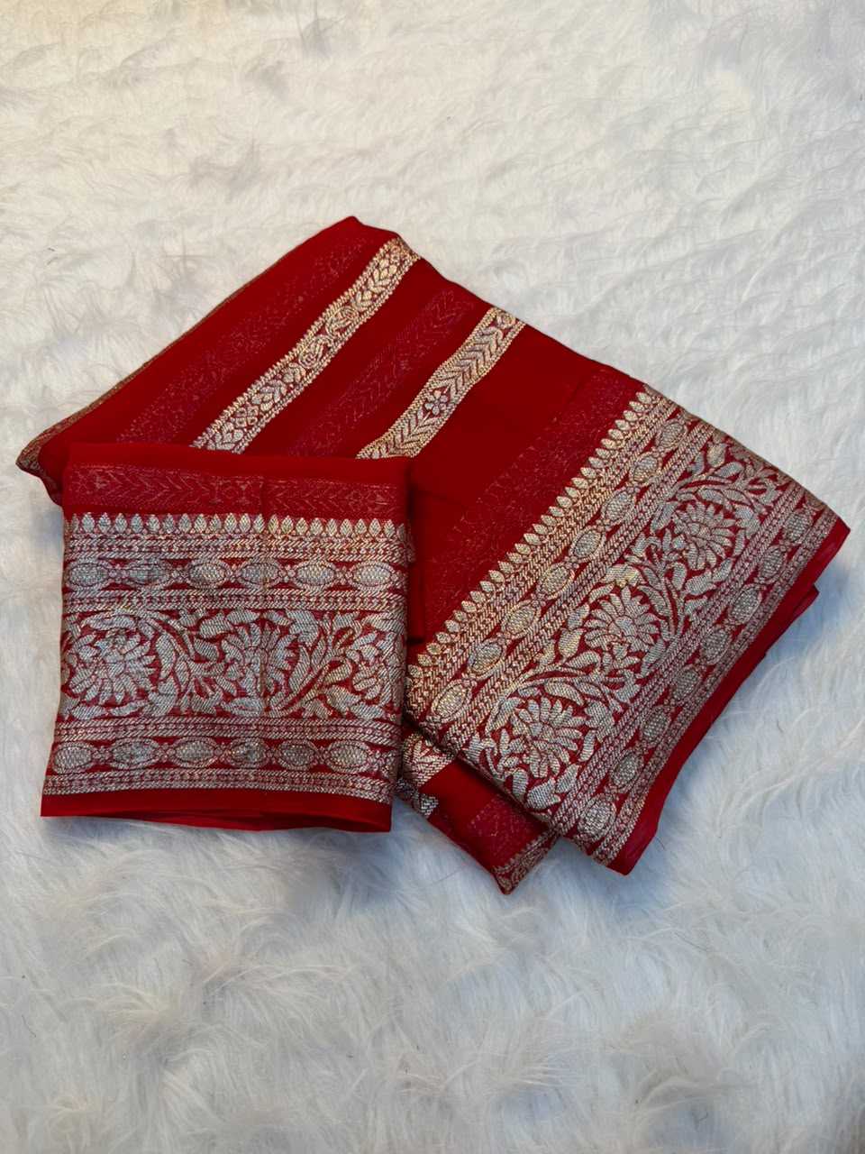 A folded red fabric item, likely a dupatta or scarf, featuring intricate silver floral and geometric patterns, displayed on a white faux fur surface.