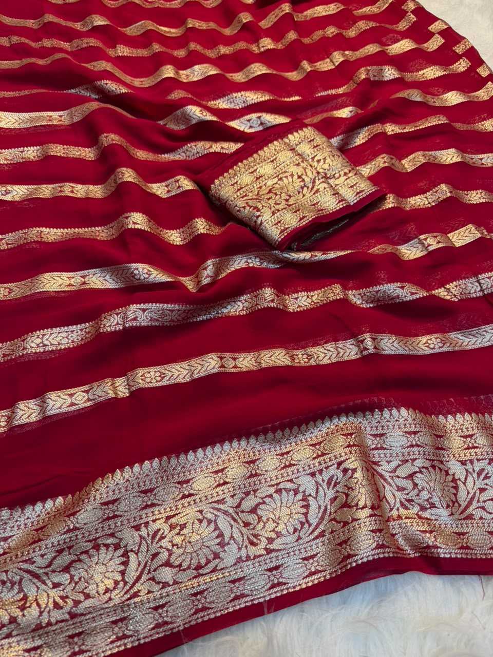 A deep red silk saree with intricate gold zari woven patterns, featuring horizontal metallic bands and a wide floral border.