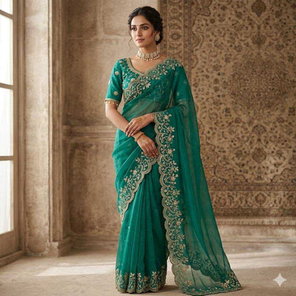 Woman wearing a teal saree with intricate embroidery in an elegant room.