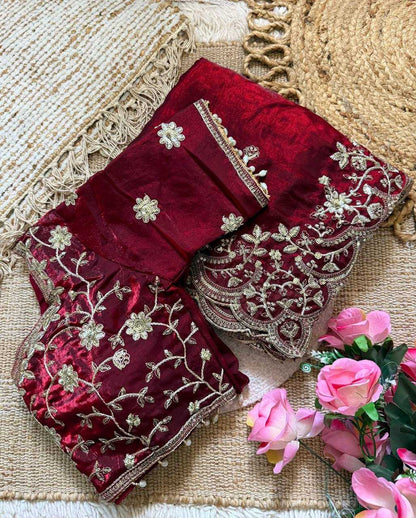 Maroon saree with silver embroidery on a textured surface with pink flowers.