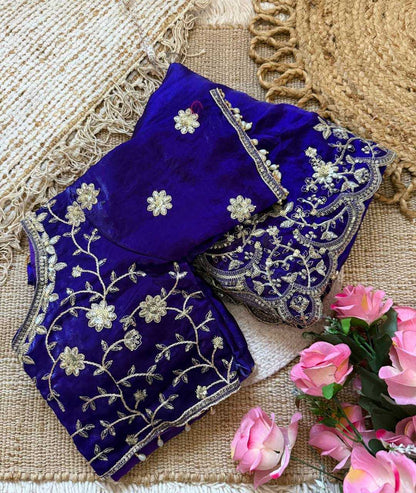 Blue embroidered blouse with floral patterns on a textured surface with pink flowers.