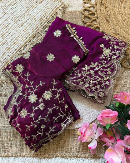 Purple embroidered saree with floral patterns on a textured surface with flowers.