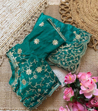 Teal embroidered fabric with gold patterns on a textured surface with pink flowers.