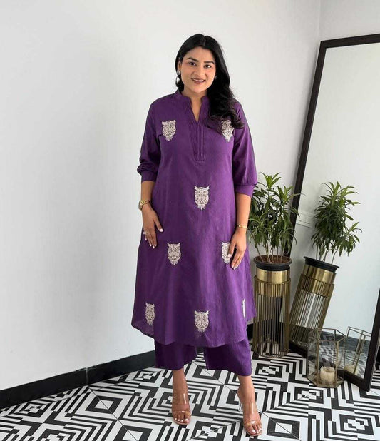 Woman wearing a purple dress with white patterns standing in a room with a mirror and plants.