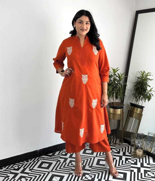 Woman wearing an orange dress with white patterns in a room with plants and a geometric floor.
