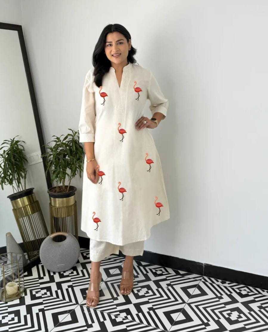 Woman wearing a white kurta with red flamingo patterns in a room with decorative plants and a mirror.