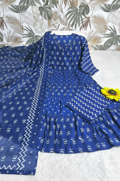 A royal blue tiered kurta set with white block prints and a matching dupatta, laid flat on a white textured surface with a tropical patterned backdrop. A 'M AND L' label is visible in the top left corner.