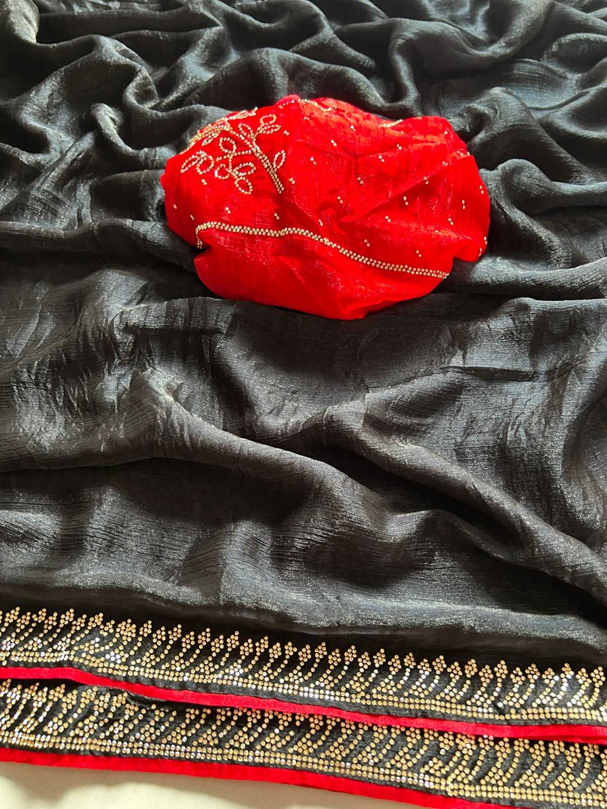 A dark gray or black sheer fabric with a decorative border, draped to show its texture and pattern, with a bright red embroidered fabric piece placed on top.
