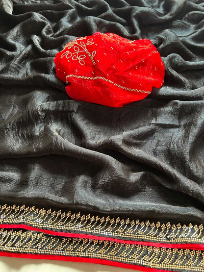 A dark gray or black sheer fabric with a decorative border, draped to show its texture and pattern, with a bright red embroidered fabric piece placed on top.