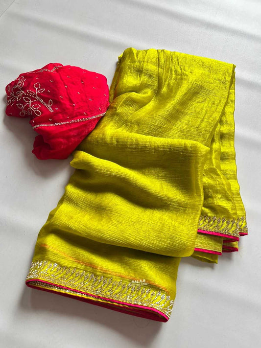 A folded bright yellow saree with a red blouse piece featuring silver embroidery, displayed on a white background.