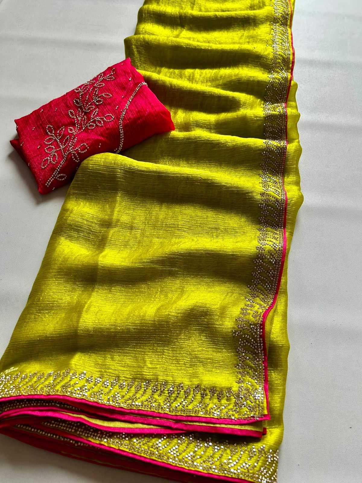 A bright yellow-green silk saree with a pink border and silver zari embroidery, paired with a matching pink blouse piece featuring white embroidery, laid out on a white surface.