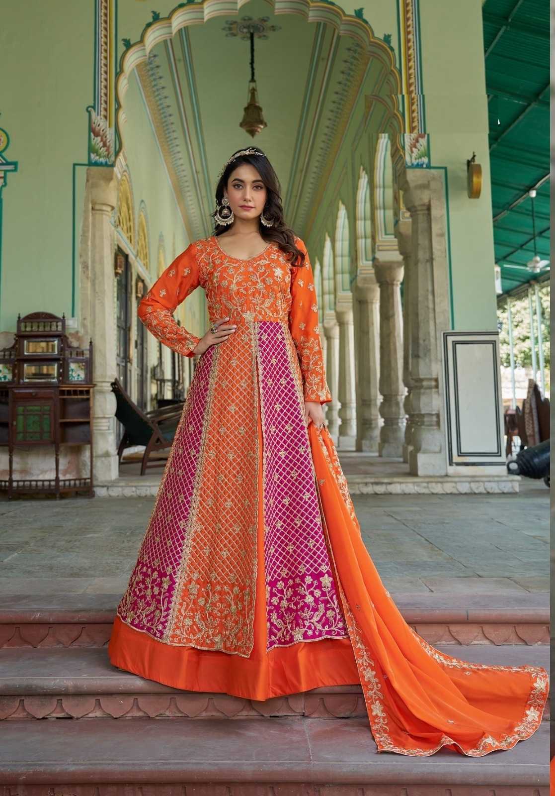 Woman in an orange and pink embroidered traditional outfit standing in a decorative architectural setting.