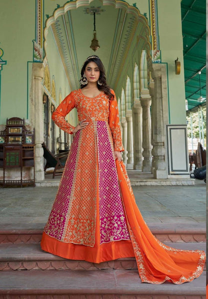 Woman in an orange and pink embroidered traditional outfit standing in a decorative architectural setting.