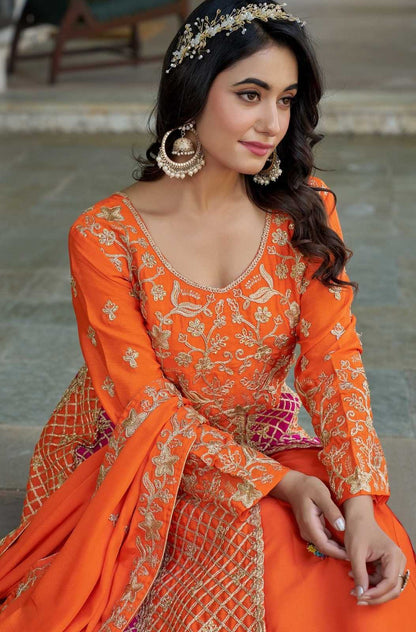 Woman in an orange traditional outfit with intricate patterns, sitting outdoors.