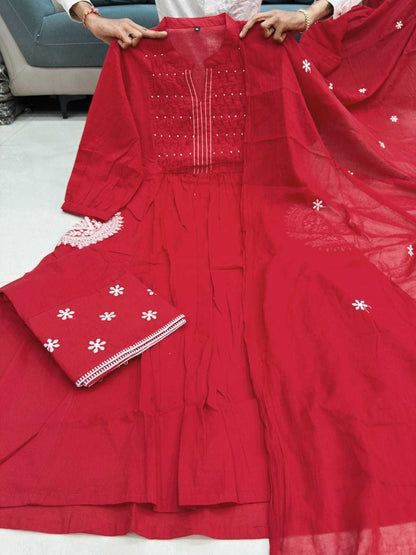 A bright red three-piece women's ethnic suit set, including a kurta with white floral embroidery and mirror work, matching flared pants, and a sheer dupatta with white embroidered motifs. Hands are holding the kurta to display it.