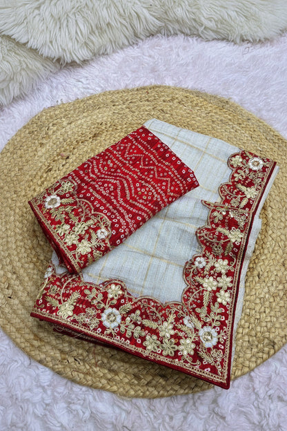 A folded red and off-white fabric set with intricate gold floral embroidery and scalloped borders, displayed on a woven straw mat over a white textured surface.