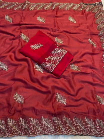 A red fabric saree or scarf with metallic gold leaf embroidery scattered across it, featuring a decorative gold border along the edges and a matching folded red fabric piece with embroidered details placed on top.