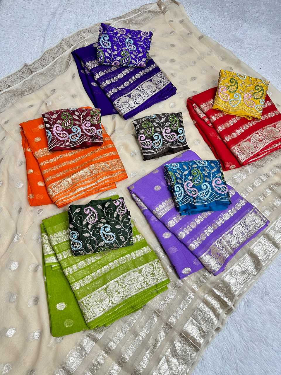A collection of folded colorful fabric pieces with ornate metallic borders and paisley embroidery, arranged on a beige patterned dupatta over a white textured surface.