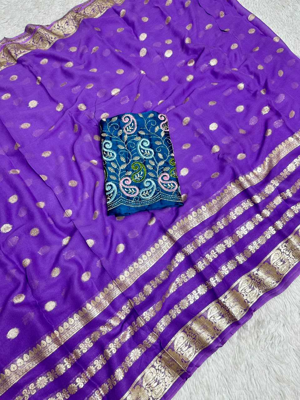 Purple silk saree with scattered metallic gold dots, a wide striped border with gold zari work, and a folded blue embroidered fabric piece placed on top.