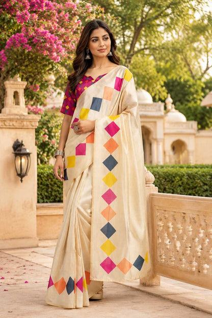 Woman in a colorful saree standing outdoors with greenery and architecture in the background