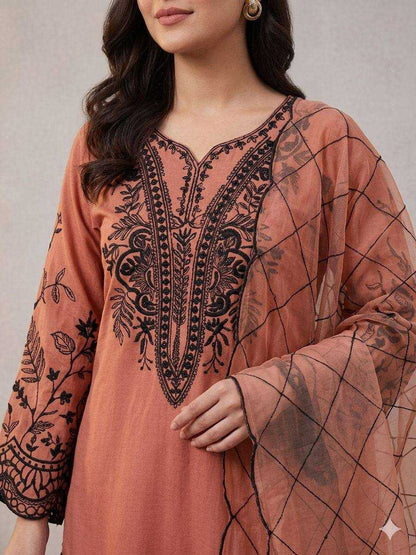 Woman wearing a peach-colored embroidered dress with black patterns on a neutral background