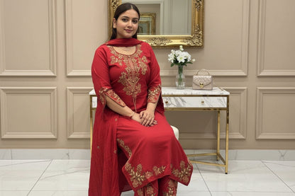 Person wearing a red embroidered traditional outfit in a decorated room.