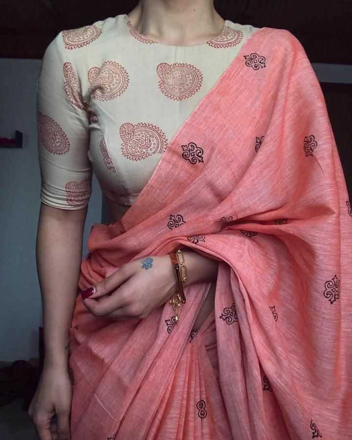 Person wearing a white blouse with red patterns and a pink saree with black designs.