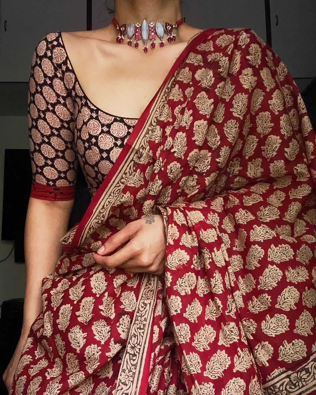 Red and gold patterned saree with a black blouse, held by a person.