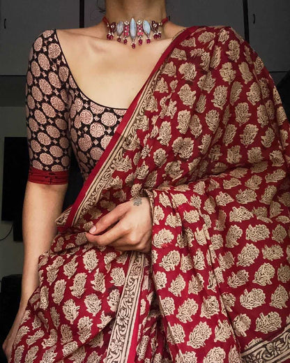 Red and gold patterned saree with a black blouse, held by a person.