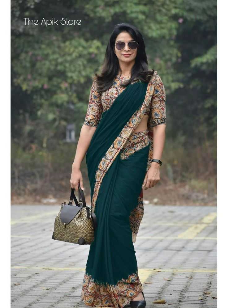 Woman wearing a green saree with a patterned blouse, holding a handbag, standing outdoors.
