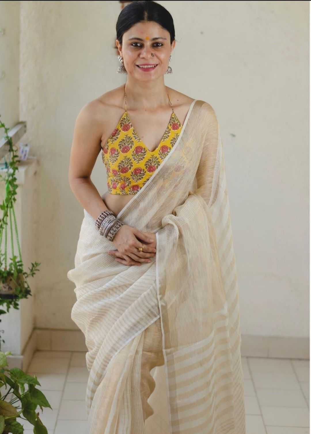 Woman wearing a floral top and beige saree indoors.