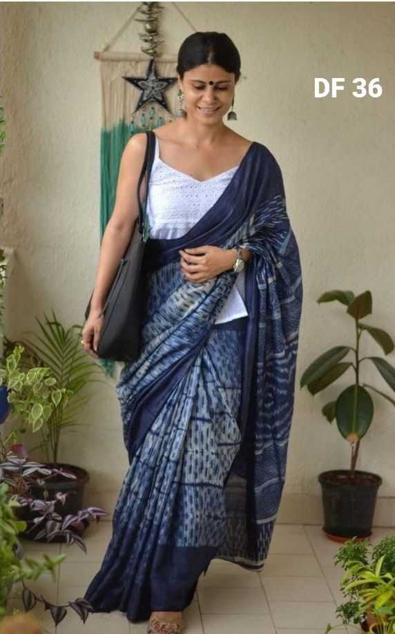 Woman wearing a blue saree with a white blouse in a home setting with plants.