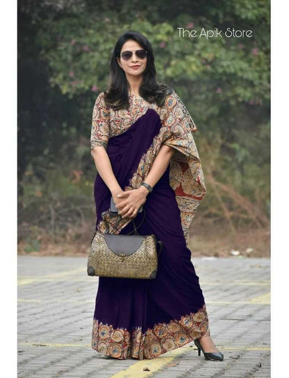 Woman in a purple saree with a patterned blouse holding a handbag, standing outdoors.