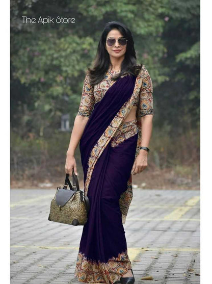 Woman wearing a purple saree with a patterned blouse, standing outdoors.