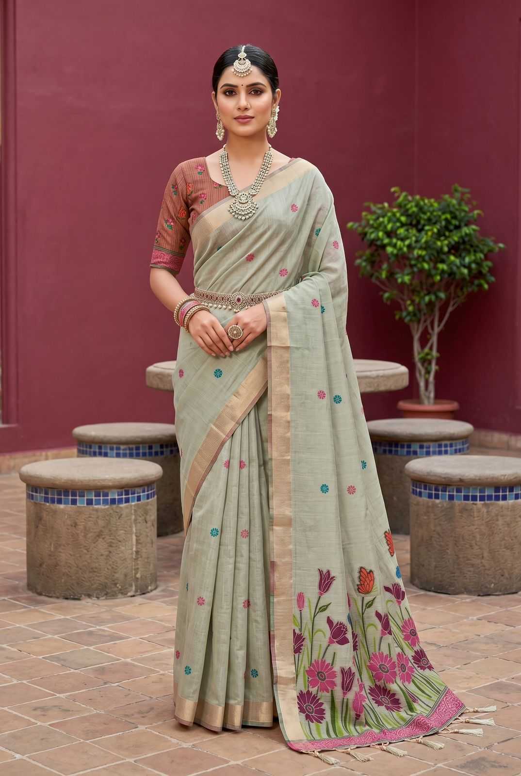 Woman in a traditional saree with floral patterns standing against a red wall.