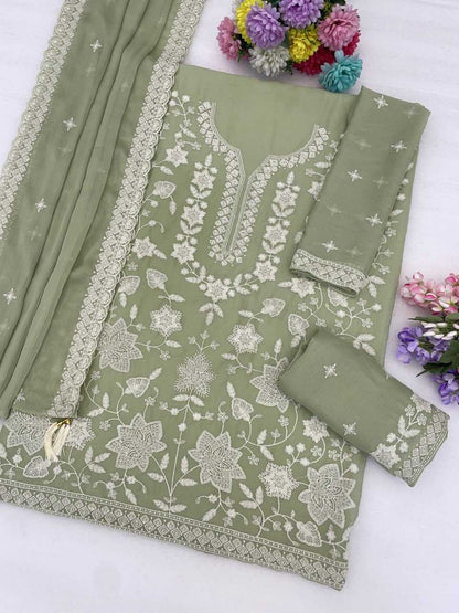 An olive green three-piece salwar kameez suit set with intricate white floral embroidery, displayed on a white background with decorative flowers.