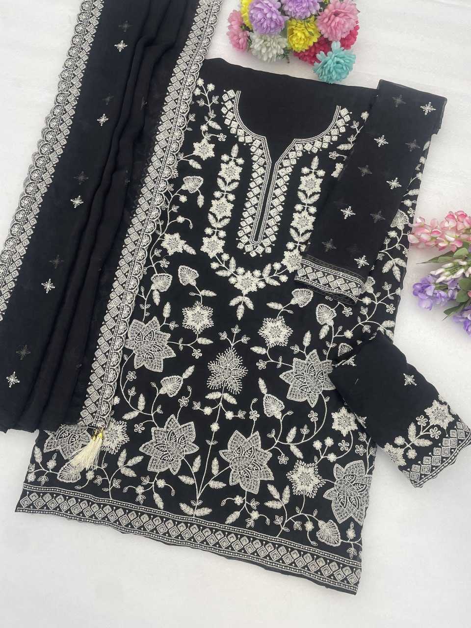 Black cotton three-piece salwar suit set with intricate silver floral embroidery, featuring a kurta, matching trousers, and a dupatta with silver borders and star motifs, styled on a white surface with decorative flowers.