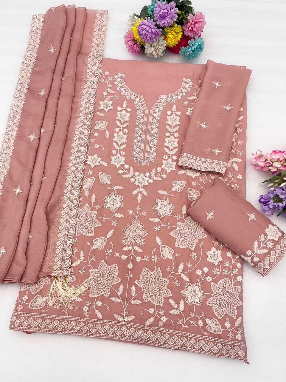 A dusty rose pink salwar suit set with intricate white floral embroidery, featuring a kurta, two matching pants, and a dupatta, styled with decorative flowers on a white background.