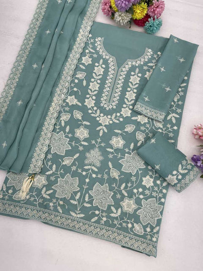 A sage green salwar suit set with intricate white floral embroidery, featuring a kurta, two matching pants, and a dupatta, styled on a light surface with decorative flowers.