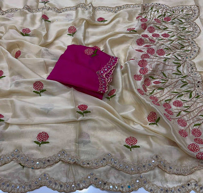 An off-white silk saree with pink and green floral embroidery and a scalloped mirror-work border, displayed with a folded magenta blouse piece.