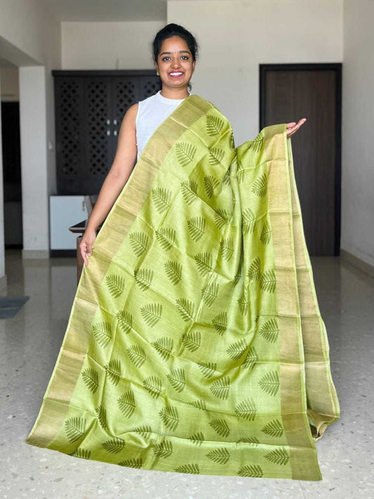 Woman holding a green saree with a leaf pattern in an indoor setting