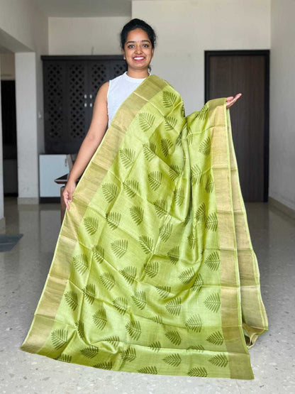 Woman holding a green saree with a leaf pattern in an indoor setting